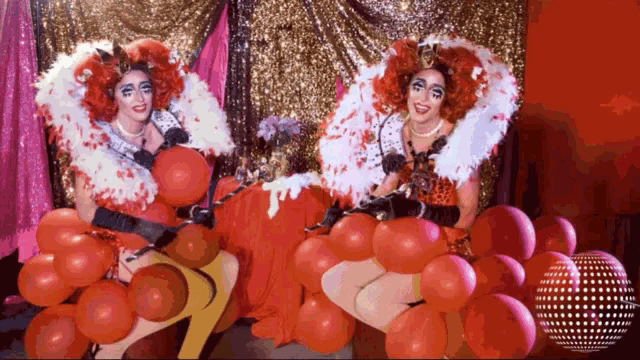 two drag queens are posing with red balloons in front of a disco ball