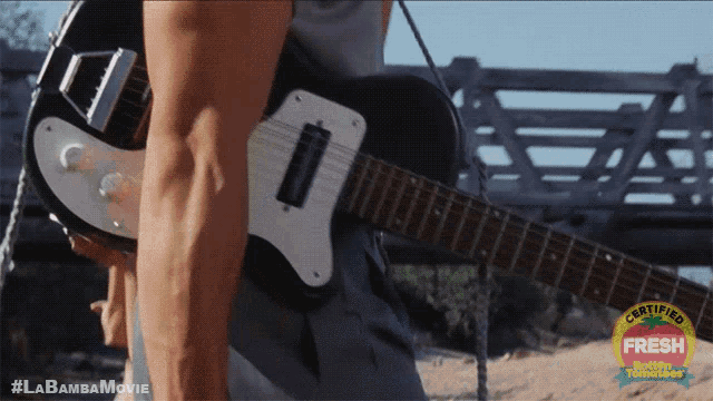 a man is holding a guitar in front of a sign that says certified fresh on it