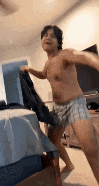 a shirtless man in plaid shorts is dancing in a room