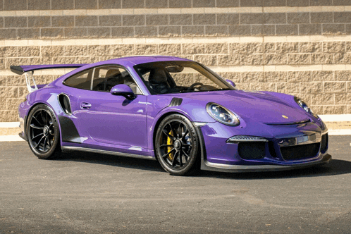 a purple car is parked in front of a brick wall