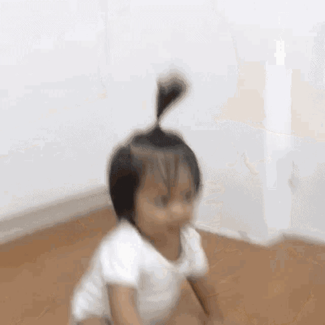 a baby is crawling on the floor with a ponytail in his hair .