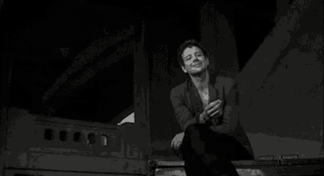 a man is smoking a cigarette while sitting on a dumpster .