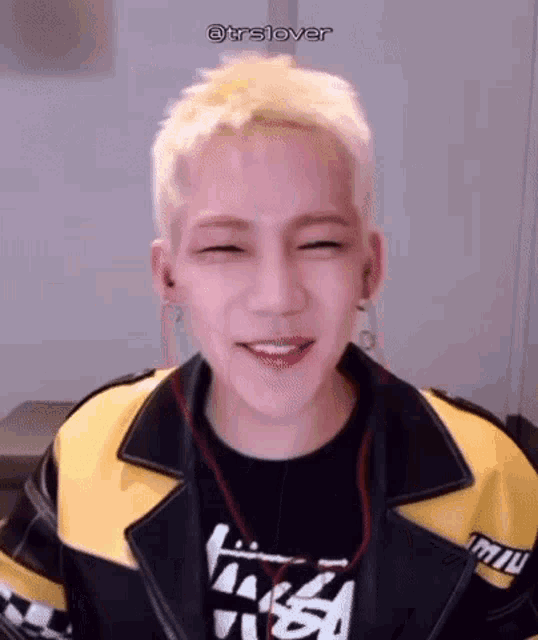a young man with blonde hair is wearing a yellow jacket and a black shirt .