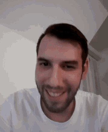 a man with a beard is smiling for the camera while wearing a white t-shirt .