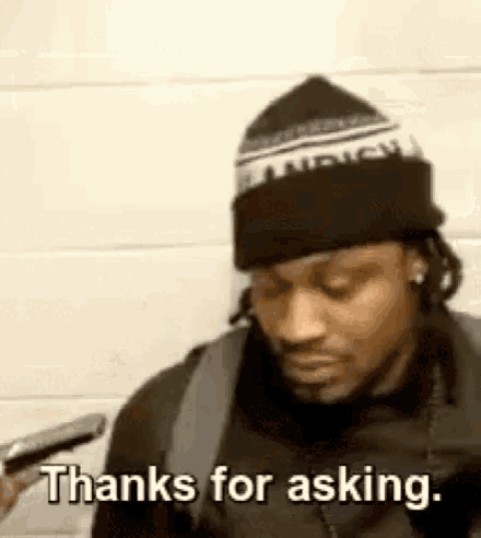 a man wearing a hat and a backpack is holding a cell phone and says `` thanks for asking . ''
