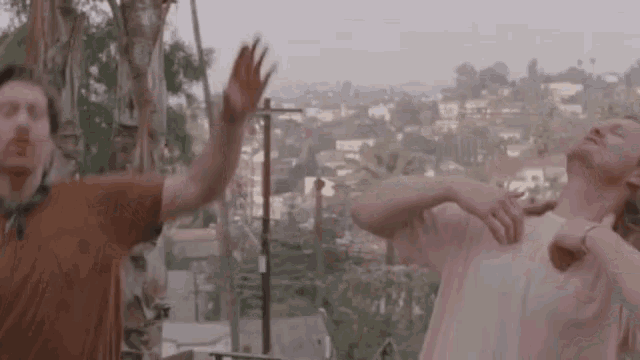 two men are standing next to each other on a balcony and giving each other a high five .