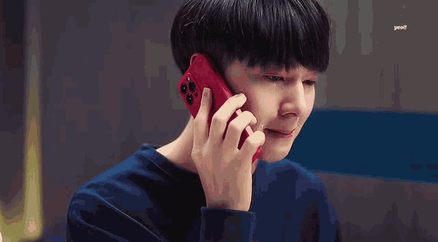 a young man crying while talking on a red phone
