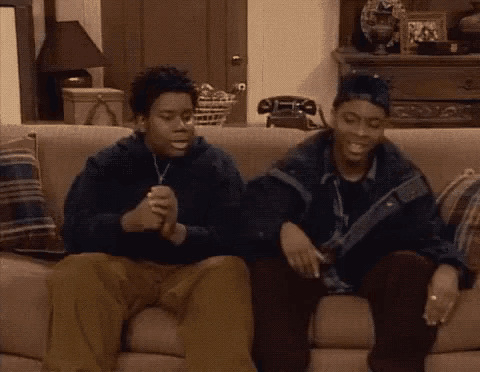 two men are sitting on a couch talking to each other and smiling .