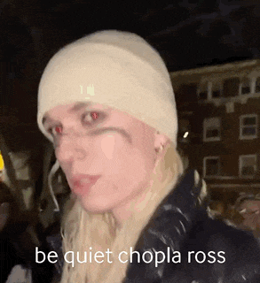 a woman wearing a white beanie and red eyes is standing in front of a building at night .