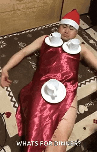a man wearing a santa hat and a red dress is laying on a bed with plates and cups around his neck .