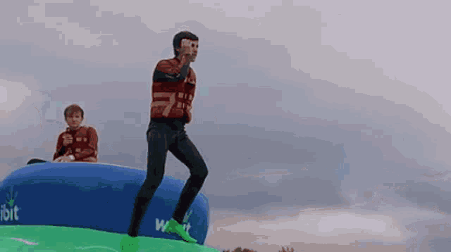 a man is jumping on a blue and green inflatable which says wait