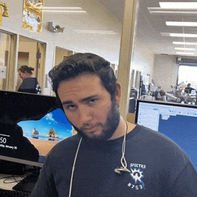 a man wearing a spectre shirt is standing in front of a computer