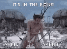 a man without a shirt is standing in the snow holding a sword and saying `` it 's in the bone '' .