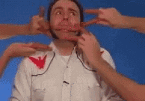 a man in a white shirt with a red eagle on the collar is being touched by a bunch of hands .