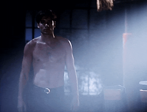 a shirtless man stands in a dark room with a belt around his waist