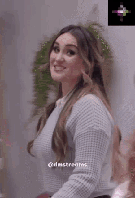 a woman wearing a grey sweater is smiling and standing in front of a shelf ..