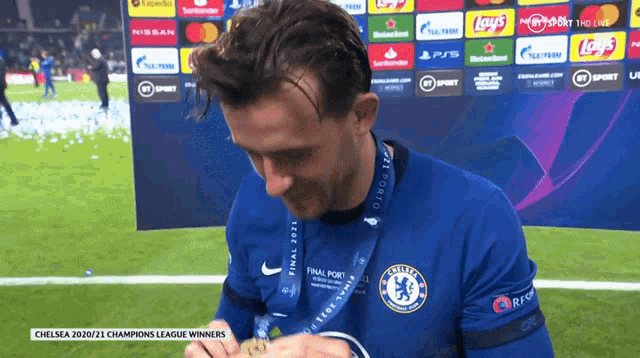 a man wearing a chelsea shirt is holding a gold medal
