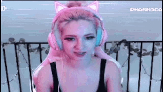 a woman wearing pink headphones with cat ears on her head is sitting in a chair .