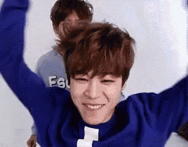 a young man in a blue sweater is smiling with his arms in the air and another man is behind him .
