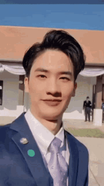 a young man in a suit and tie is standing in front of a building and smiling .
