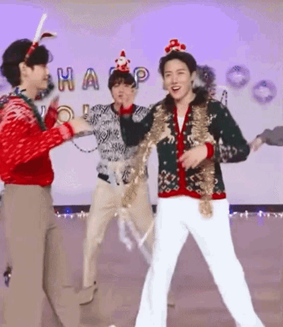 a group of men are dancing together on a stage while wearing christmas sweaters .