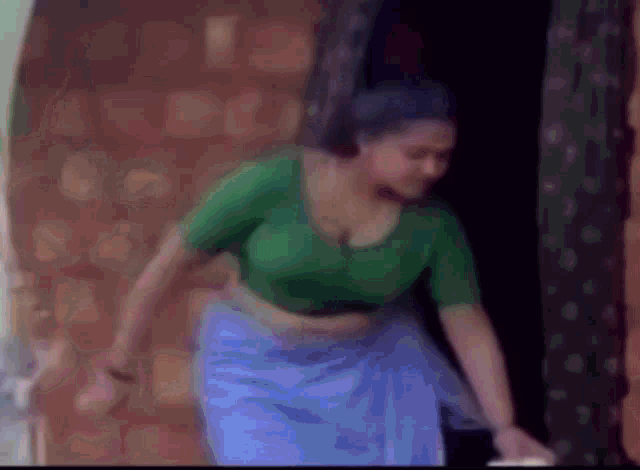 a woman in a green blouse and a blue skirt is standing in a doorway .