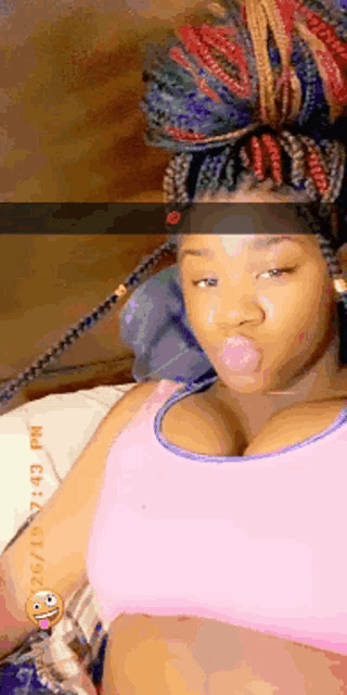 a woman with braids is laying on a bed and blowing a bubble with her tongue out .