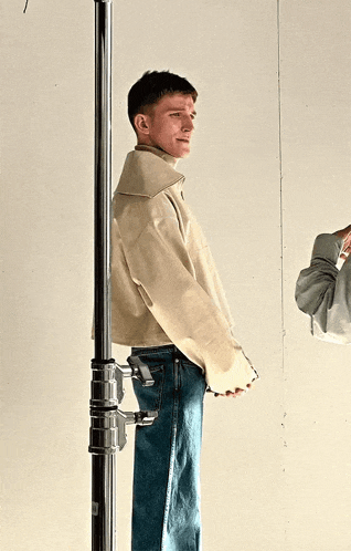 a man wearing a white jacket and blue jeans is standing next to a metal pole