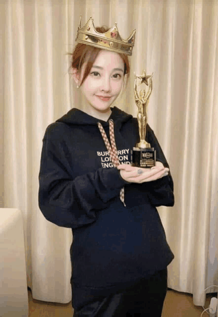 a woman wearing a black burberry sweatshirt holds a trophy