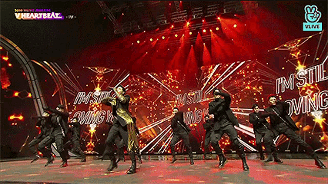 a group of men are dancing on a stage and the words i 'm still loving are on the screen behind them