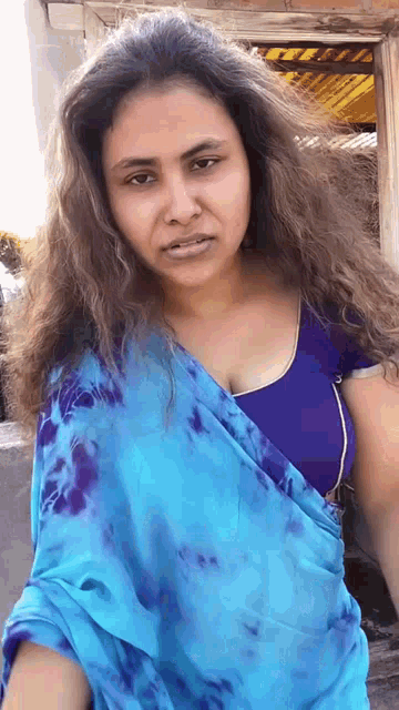 a woman wearing a blue saree and a blue top is standing in front of a building .