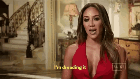 a woman in a red dress is standing in front of a staircase and talking .