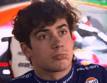a young man with curly hair is wearing a gulf shirt and making a face .