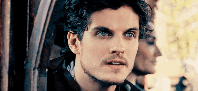 a man with a beard and blue eyes is looking at a woman in a mirror .