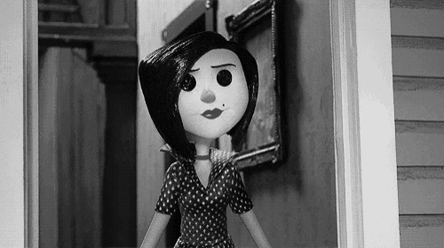 a black and white photo of a cartoon doll in a polka dot dress standing in a doorway .