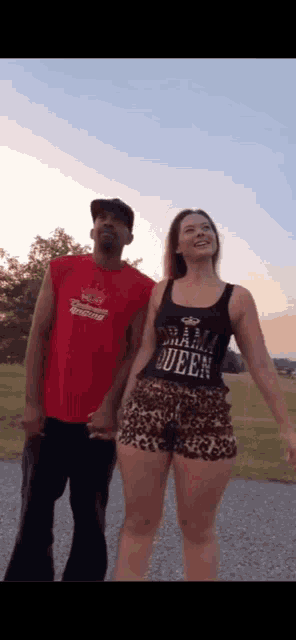 a man and a woman are holding hands and the woman is wearing a black tank top that says queen