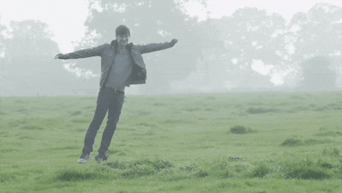 a man with his arms outstretched is standing in a grassy field