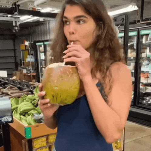 a woman drinking from a coconut with a straw