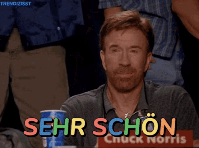 a man with a beard is sitting in front of a sign that says sehr schön