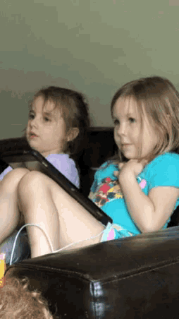 two little girls are sitting on a couch playing with their phones