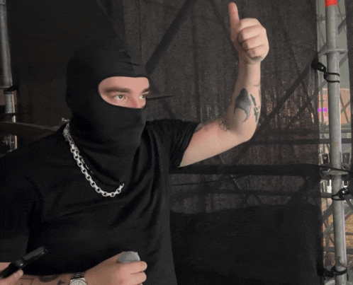 a man wearing a black mask is giving a thumbs up sign