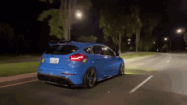 a blue car is driving down a street at night with a yellow sticker on the back that says ' california ' on it