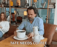 a man is sitting at a table with a stack of cups of coffee on it .