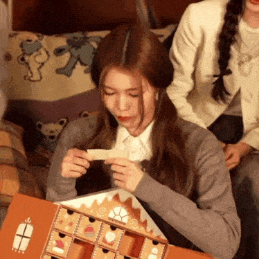 a girl is opening a gingerbread house shaped box