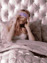 a woman is laying in bed with a purple eye mask on her eyes .
