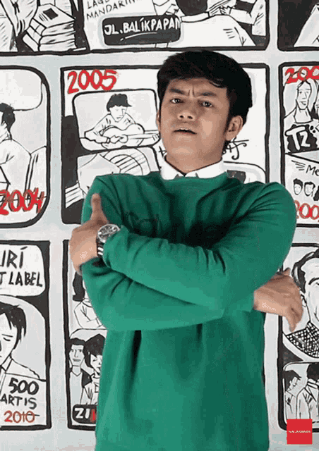 a man in a green sweater is standing in front of a wall with cartoons on it