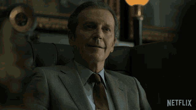a man in a suit and tie sits in a chair with netflix written on the bottom