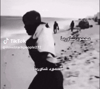 a black and white photo of a man walking on a beach with arabic writing .