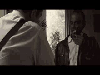 a man in a leather jacket is smoking a cigarette while talking to another man .