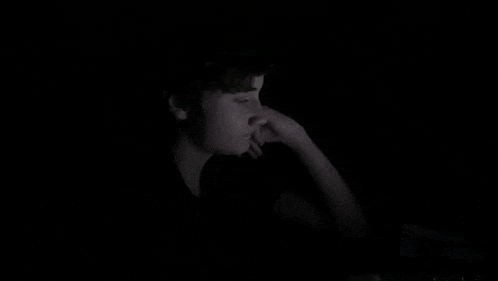 a man is sitting in the dark looking at a computer screen .